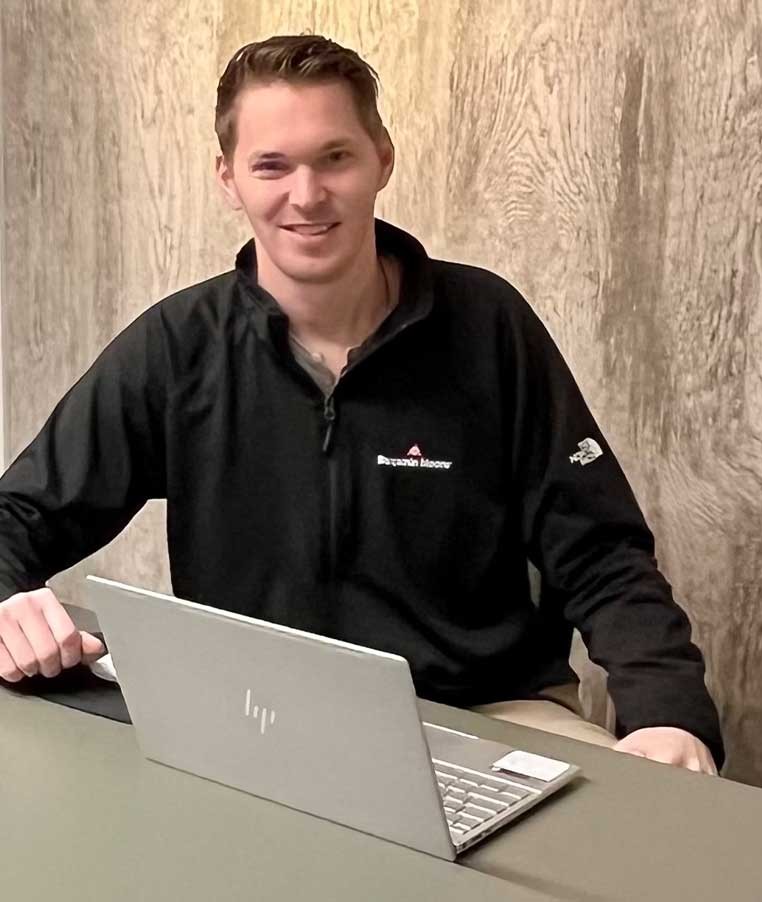 A young man in a black shirt sitting at a desk with a laptop